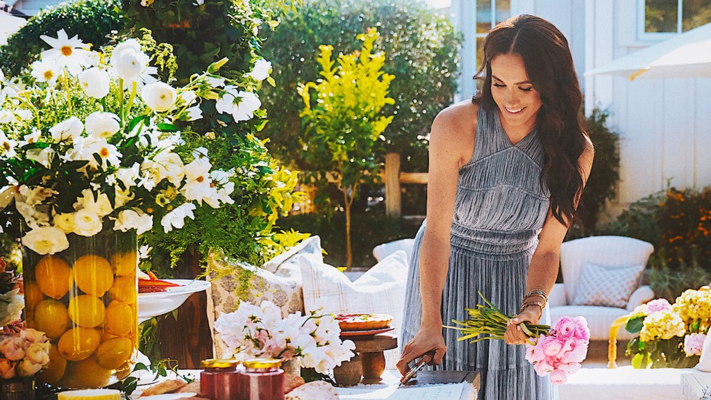 Meghan Markle in a grey dress, holding flowers.