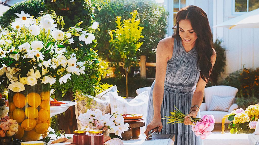 Meghan Markle in a grey dress, holding flowers.