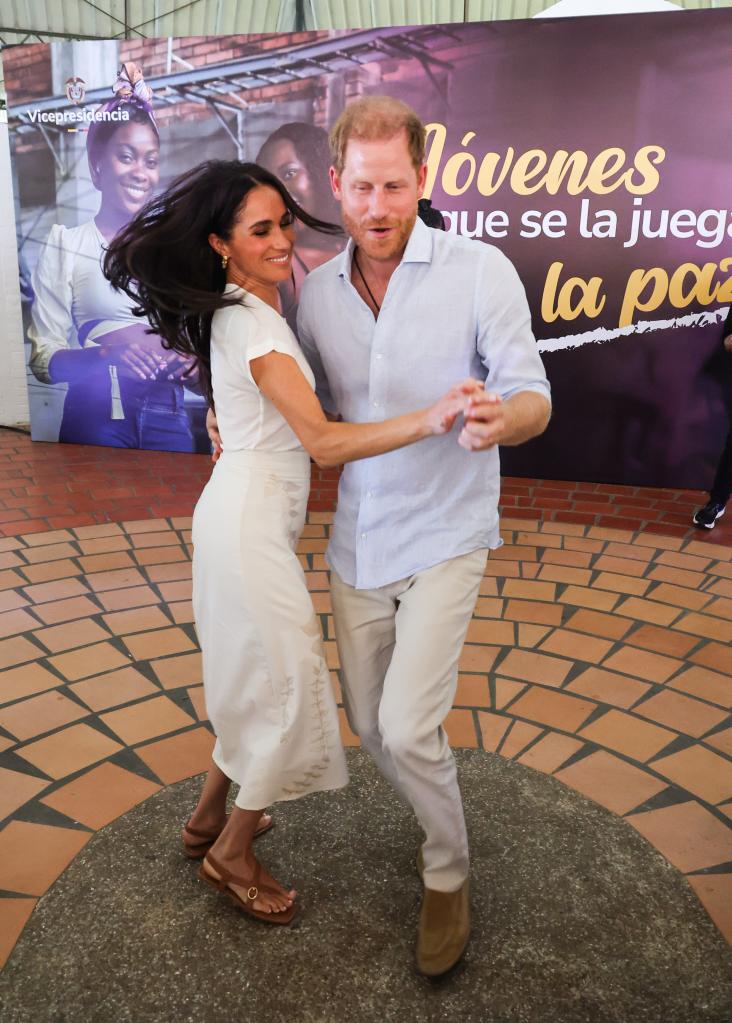 Meghan Markle, in a cream dress, dances with Prince Harry, in cream pants and a white shirt.